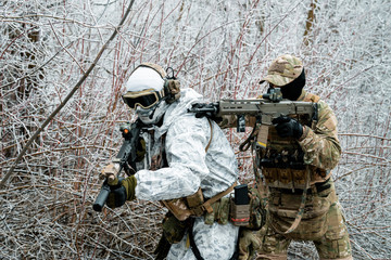 Wall Mural - Two men in camouflage white, green uniform with machineguns. Soldiers with muchineguns go one after another in the winter forest. Horizontal photo