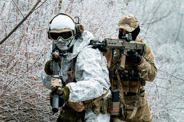 Wall Mural - Closeup two men in camouflage white, green uniform with machineguns. Soldiers with muchineguns go one after another in the winter forest.