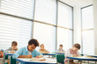 © AnnaStills - Horizontal shot of young middle school students sitting at desks in modern classroom doing lesson exercises, copy space