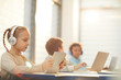 © AnnaStills - Middle school students sitting in classroom using modern headphones and computers during lesson, horizontal shot, copy space