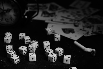 Dice,cigarettes, cards, and an abandoned alarm clock on a table in an underground casino.In black and white.