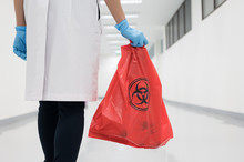Scientist Wearing Blue Gloves And Red Bag With Bioharzard Sign.A Woman Worker Hand Holding Red Garbage Bag.Maid And Infection Waste Bin At The Indoor Public Building.Infectious Control.