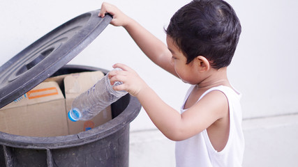 cute little asian 2 year old toddler baby boy child throwing plastic bottle in recycling trash bin a