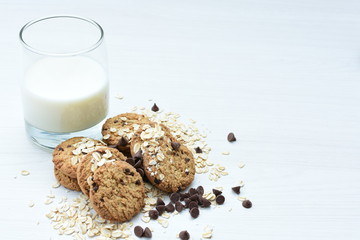 Oatmeal cookies and chocolate chips accompanied by glass of milk