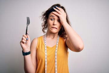 Sticker - Young beautiful woman with curly hair doing diet holding fork and tape measure stressed with hand on head, shocked with shame and surprise face, angry and frustrated. Fear and upset for mistake.