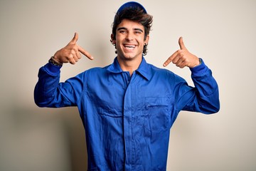 Wall Mural - Young mechanic man wearing blue cap and uniform standing over isolated white background looking confident with smile on face, pointing oneself with fingers proud and happy.