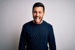 Young handsome man with beard wearing casual sweater standing over white background sticking tongue out happy with funny expression. Emotion concept.