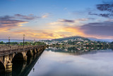 Sunset in Pontedeume, Galicia, Spain Ancient Roman stone bridge and reflections of the hill and village in the calm water. Golden clouds and colors of the sunset