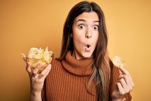 Young Beautiful Girl Holding Bowl With Chips Potatoes Standing Over Yellow Background Scared In Shock With A Surprise Face, Afraid And Excited With Fear Expression