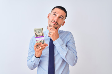 Poster - Young handsome business man holding a bunch of dollars bank notes over isolated background serious face thinking about question, very confused idea