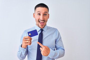 Wall Mural - Young business man holding credit card over isolated background very happy pointing with hand and finger