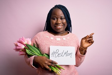 Sticker - Plus size african american woman holding best mom message and tulips on mothers day very happy pointing with hand and finger to the side