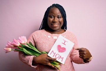 Sticker - Plus size african american woman holding love mom message and tulips on mothers day very happy pointing with hand and finger