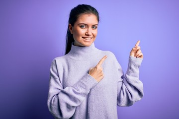 Young beautiful woman with blue eyes wearing casual turtleneck sweater over pink background smiling and looking at the camera pointing with two hands and fingers to the side.