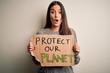 © Krakenimages.com - Young beautiful brunette activist woman protesting for protect our planet holding poster scared in shock with a surprise face, afraid and excited with fear expression