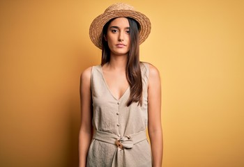 Young beautiful brunette woman on vacation wearing casual dress and hat Relaxed with serious expression on face. Simple and natural looking at the camera.