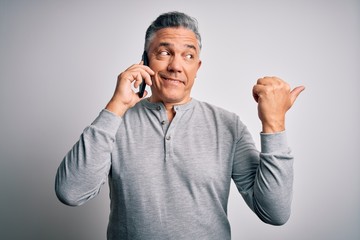 Poster - Middle age handsome grey-haired man having conversation talking on the smartphone pointing and showing with thumb up to the side with happy face smiling