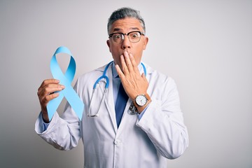 Sticker - Middle age handsome grey-haired doctor man wearing coat holding blue cancer ribbon cover mouth with hand shocked with shame for mistake, expression of fear, scared in silence, secret concept