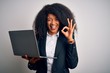 Young african american business woman with afro hair using computer laptop from job doing ok sign with fingers, excellent symbol