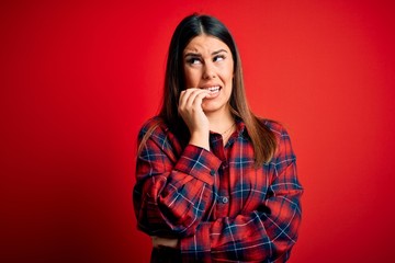 Sticker - Young beautiful woman wearing casual shirt over red background looking stressed and nervous with hands on mouth biting nails. Anxiety problem.