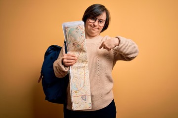 Sticker - Young down syndrome tourist woman wearing bag and looking at destination city map with surprise face pointing finger to himself