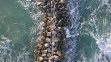 Aerial View Of A Fishermen Are Standing On A Breakwater And Waves Crashing On The Breakwater.