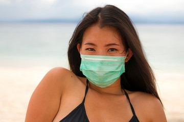 use of medical face mask in public places- young attractive Asian Chinese woman enjoying beach holidays in bikini and protective facial mask in prevention vs virus infection