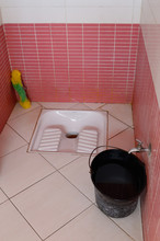 Pink And White Tiled Mens Restroom With Squat Toilet Fixture And Bucket In Morocco