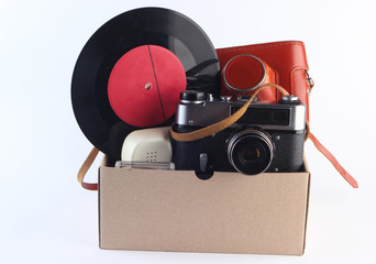 Cardboard box with retro film camera, gamepad,  vinyl record, phone tube on a white background. Antiques, trash