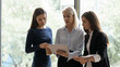 © fizkes - Diverse female employees stand brainstorm discuss business project using modern tablet gadget, confident middle-aged businesswoman talk with woman coworkers in office, collaboration concept