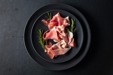 Wall Mural - Prosciutto and rosemary on a black plate. Top view.