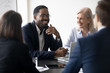Smiling multiracial diverse businesspeople sit at office desk discussing business project together, happy multiethnic colleagues coworkers brainstorm talk consider cooperation in boardroom