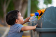 Little asian toddler baby boy throwing plastic bottle in recycling trash bin at public park