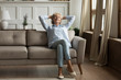 © fizkes - Relaxed mature 60s grandmother sit on couch in living room sleep, daydream or take nap, calm senior 70s woman rest relax on comfortable sofa ta home, breathe fresh air, stress free concept