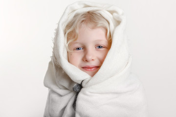 Wall Mural - Portrait of beautiful smiling Caucasian girl wrapped in white blanket. Happy preschool child with blue eyes covered with warm woolen shawl on a light background. Positive emotion face expression.