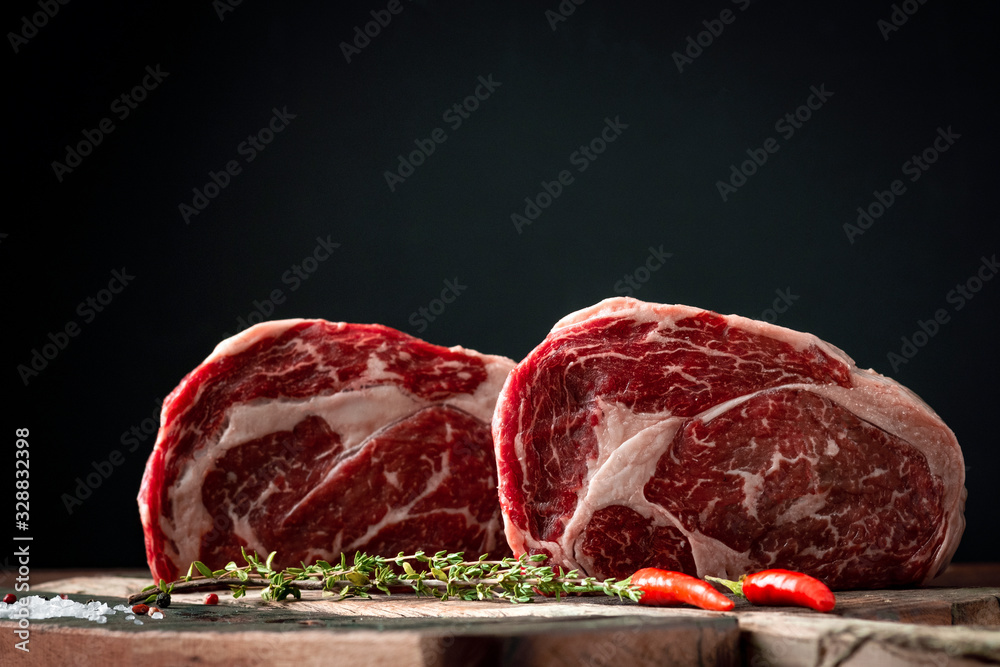 Raw rib eye beef steak with pepper and herbs on a wooden background in a butcher shop - obrazy, fototapety, plakaty 