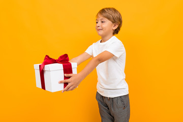 Wall Mural - Cute little boy in t-shirt and trousers holds a box with gift himself isolated on yellow background