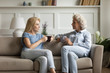 © fizkes - Happy senior mother and grownup daughter sit relax on couch in living room talk drinking tea or coffee together, mature mum and adult girl child rest on sofa, enjoy family weekend at home chatting