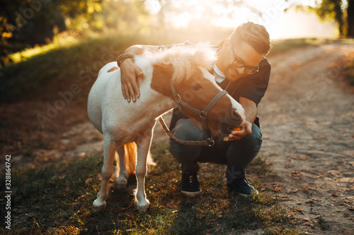 Fotomural Young attractive male veterinarian examining and feeding adorable little pony horse