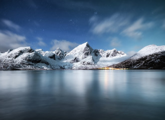 Mountains and reflections on water at night. Winter landscape. The sky with stars and clouds in motion. Nature as a background. Norway - travel