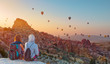 © muratart - Hot air balloon flying over spectacular Cappadocia - Girls watching hot air balloon at the hill of Cappadocia