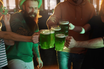 Wall Mural - Group of friends toasting with green beer in pub, closeup. St. Patrick's Day celebration