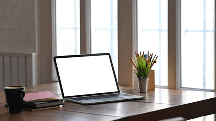 Poster - Photo of white blank screen computer putting on wooden table together with potted plant, coffee cup, coffee cup, stack of books. Vintage style workplace concept.