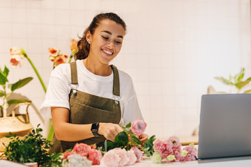 Wall Mural - Smiling woman working in her flower shop. Female florist arranging flowers on the counter.