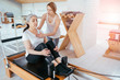 Brunette female instructor with cute two braids hairstyle consulting hansdome beard man workout pilates on reformer practice in pilates studio, working out indoor, correcting beginners, full length.