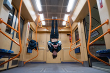 Girl Hanging By Feet Upside Down In The Subway Carriage And Using Smartphone. Concept Of Overusing Social Networks And Addiction