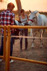 Wall Mural -   man and woman with horse at  ranch.Man prepare saddle for  horse.