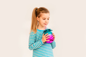 Little blonde girl is smiling on a white background. child girl in a blue jacket is holding a pineapple-shaped drink glass on a white background. summer vacation concept