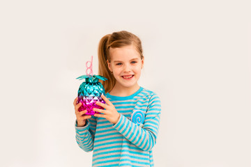 Little blonde girl is smiling on a white background. child girl in a blue jacket is holding a pineapple-shaped drink glass on a white background. summer vacation concept