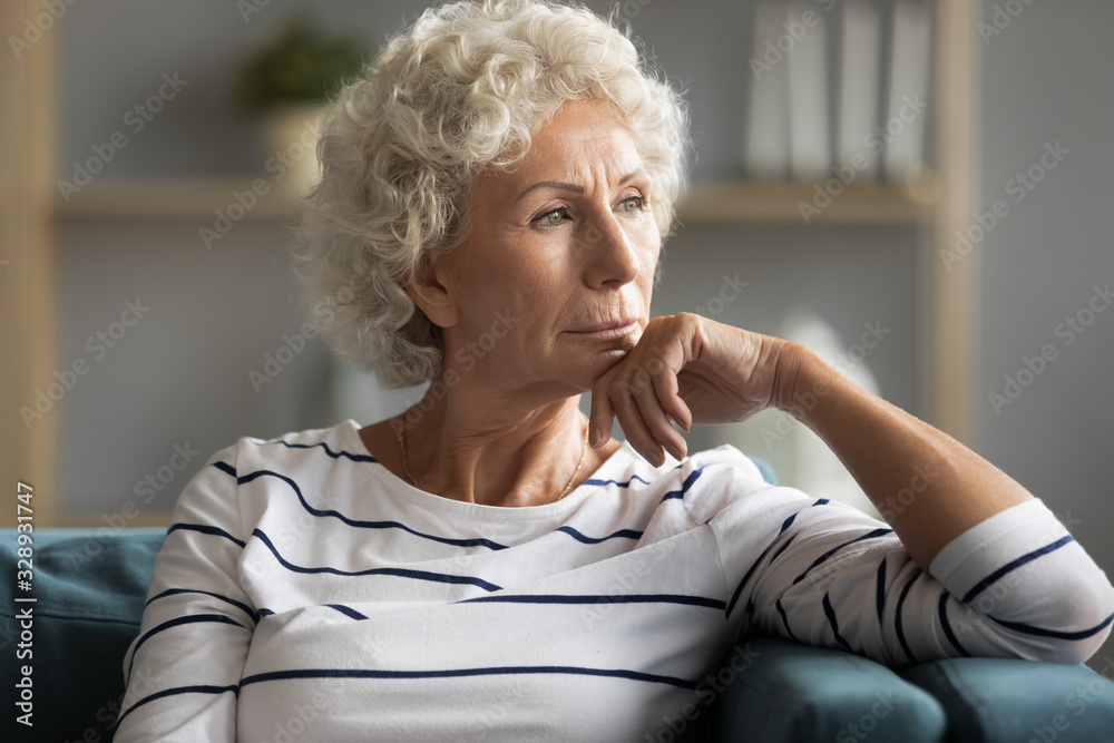 Pensive middle-aged old lady sit on couch at home look in distance thinking pondering, thoughtful unhappy elderly woman lost in thoughts missing remembering past, feeling lonely, solitude concept - obrazy, fototapety, plakaty 